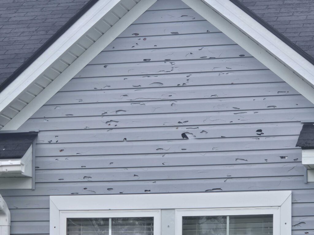 The side of a grayish-blue Denver home is significant hail damage in the siding